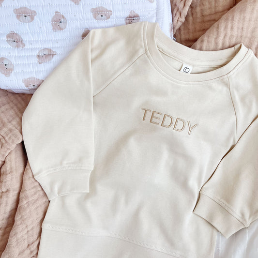 toddler crewneck pullover in natural with a simple, modern uppercase name embroidery in camel thread paired with a quilted teddy bear dopp kit