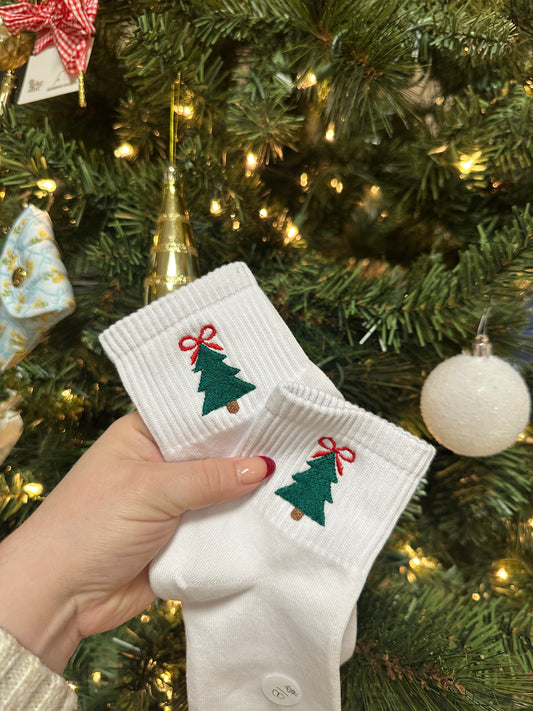 White socks with green tree designs held in front of a decorated Christmas tree.