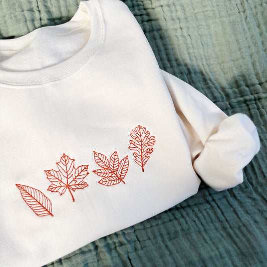 styled flat lay of a sweet cream crewneck sweatshirt with embroidered outlines stitched fall leaves in a pumpkin spice thread color