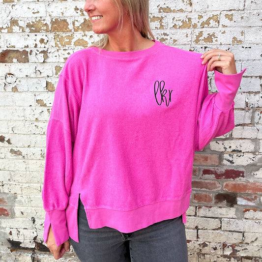 Woman wearing an oversized boxy cropped ribbed crewneck sweatshirt with split hem and cuff details in the pinkberry color. on the left chest is an embroidered monogram in black thread.