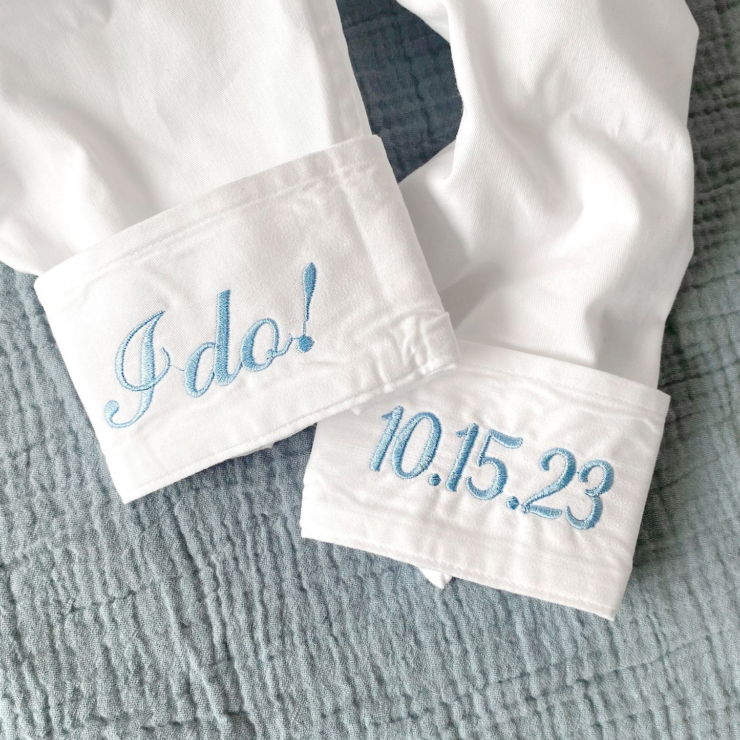 close up of cuff embroidery. on the left sleeve is I do ! and on the right sleeve is custom wedding date, both embroidered in baby blue thread