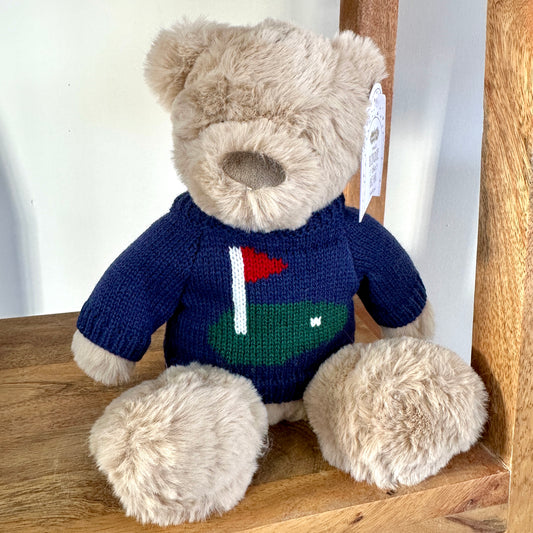 Teddy bear wearing a blue sweater with a golf design on a wooden surface
