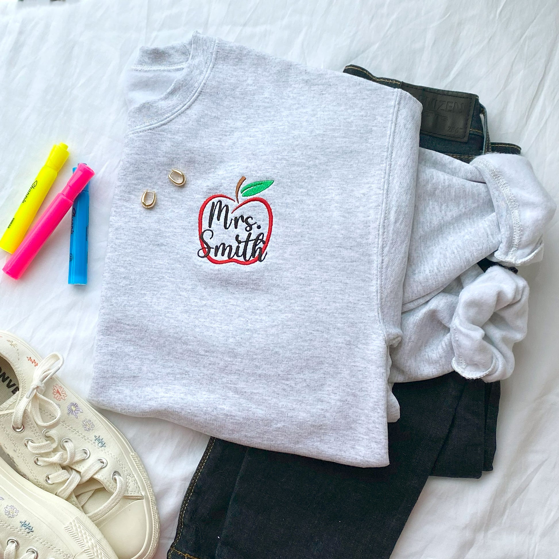 Ash crewneck sweatshirt with apple outline and custom name embroidered design styled with jeans and school supplies
