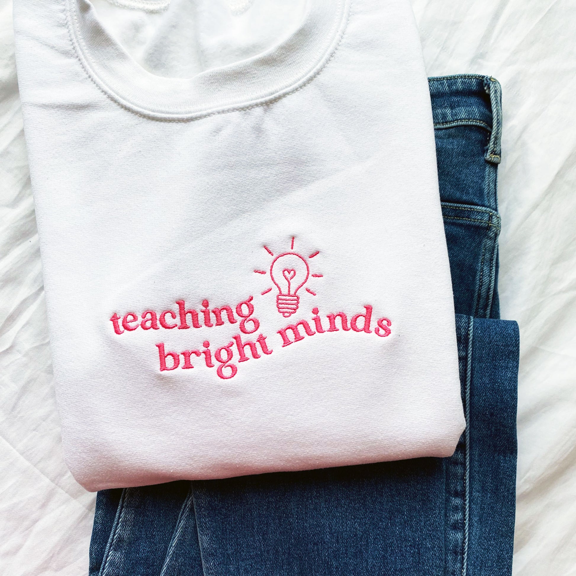 white teacher pullover sweatshirt with a teaching bright minds lightbulb embroidered design on the chest