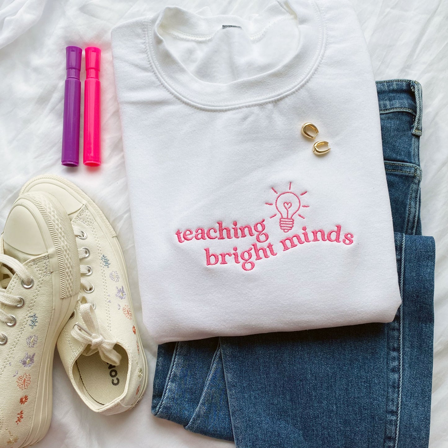 white teacher pullover sweatshirt with a teaching bright minds lightbulb embroidered design on the chest