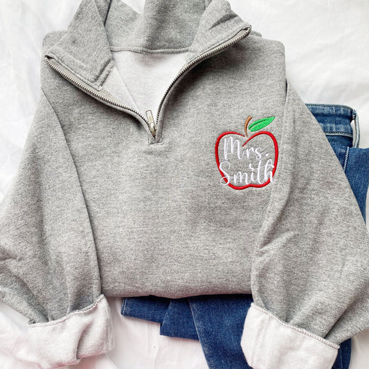oxford grey quarter zip pullover with an outlined apple design with a name over top embroidered on the left chest.