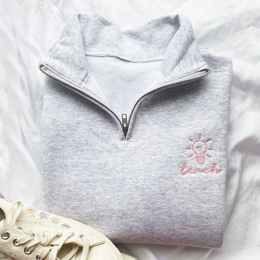 light grey pullover quarter zip with a cute lightbulb teach embroidered design on the left chest