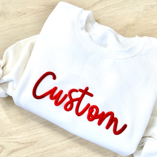 White sweatshirt with red 'Custom' text on a wooden surface