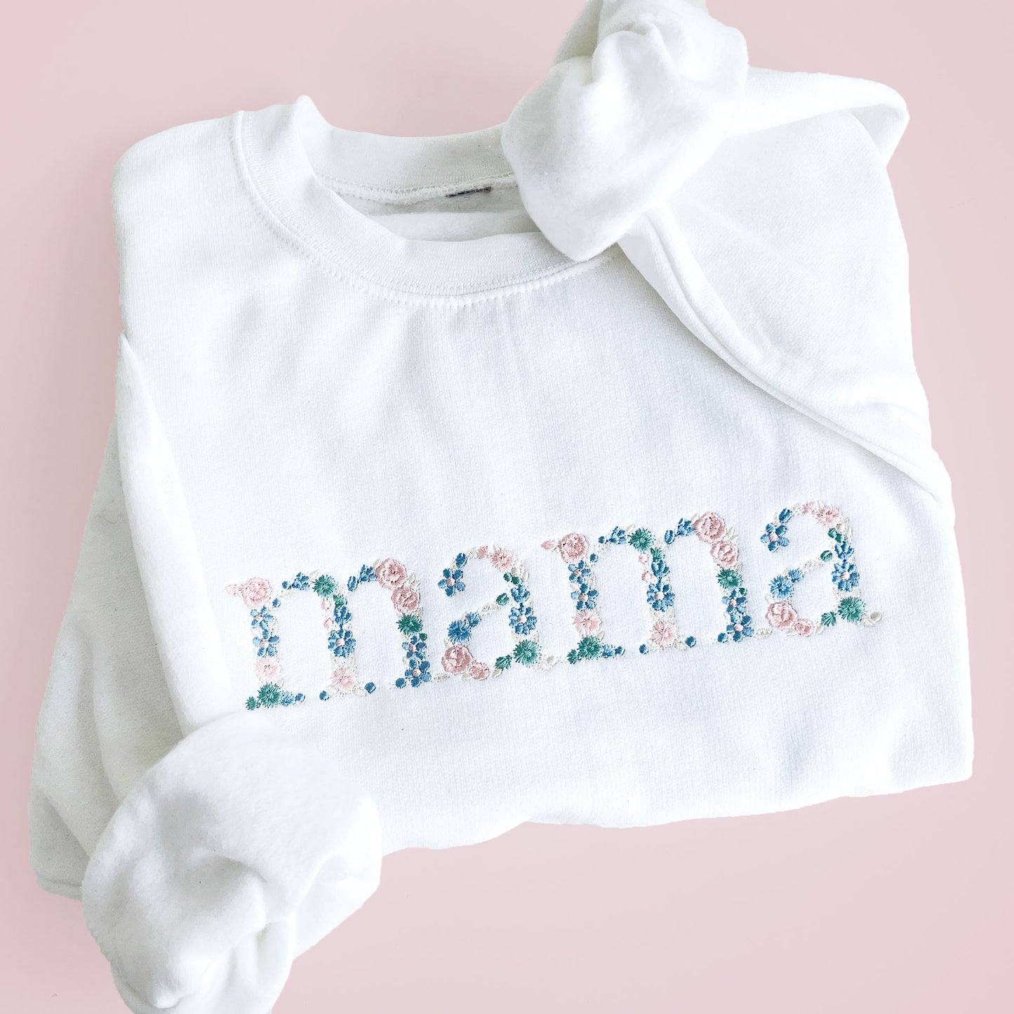 white crewneck sweatshirt with custom floral mama embroidered design in shades of blue, green, and pink