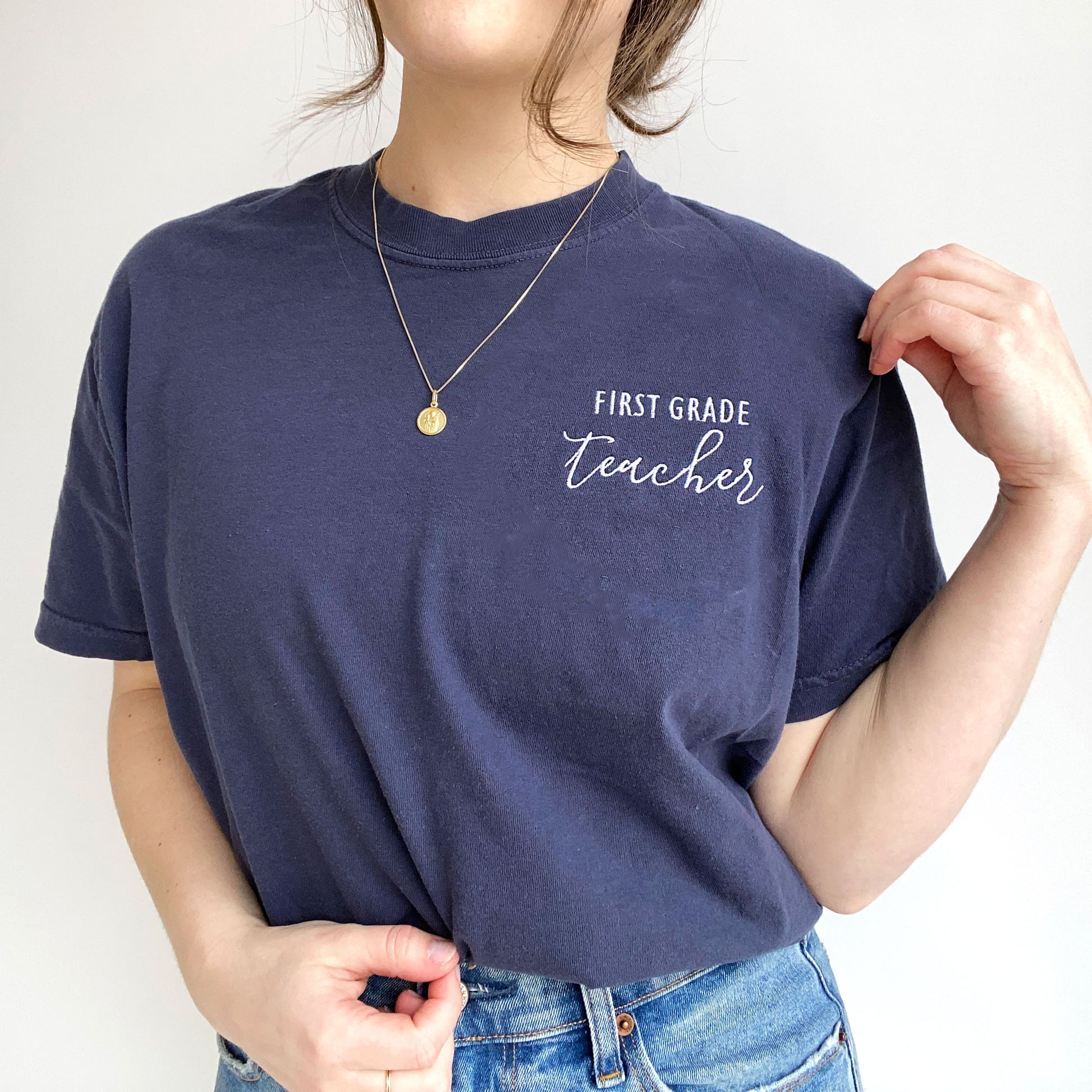 young woman modeling a nay comfort colors t-shirt with embroidered custom grade level and teacher design in white threads on the left chest