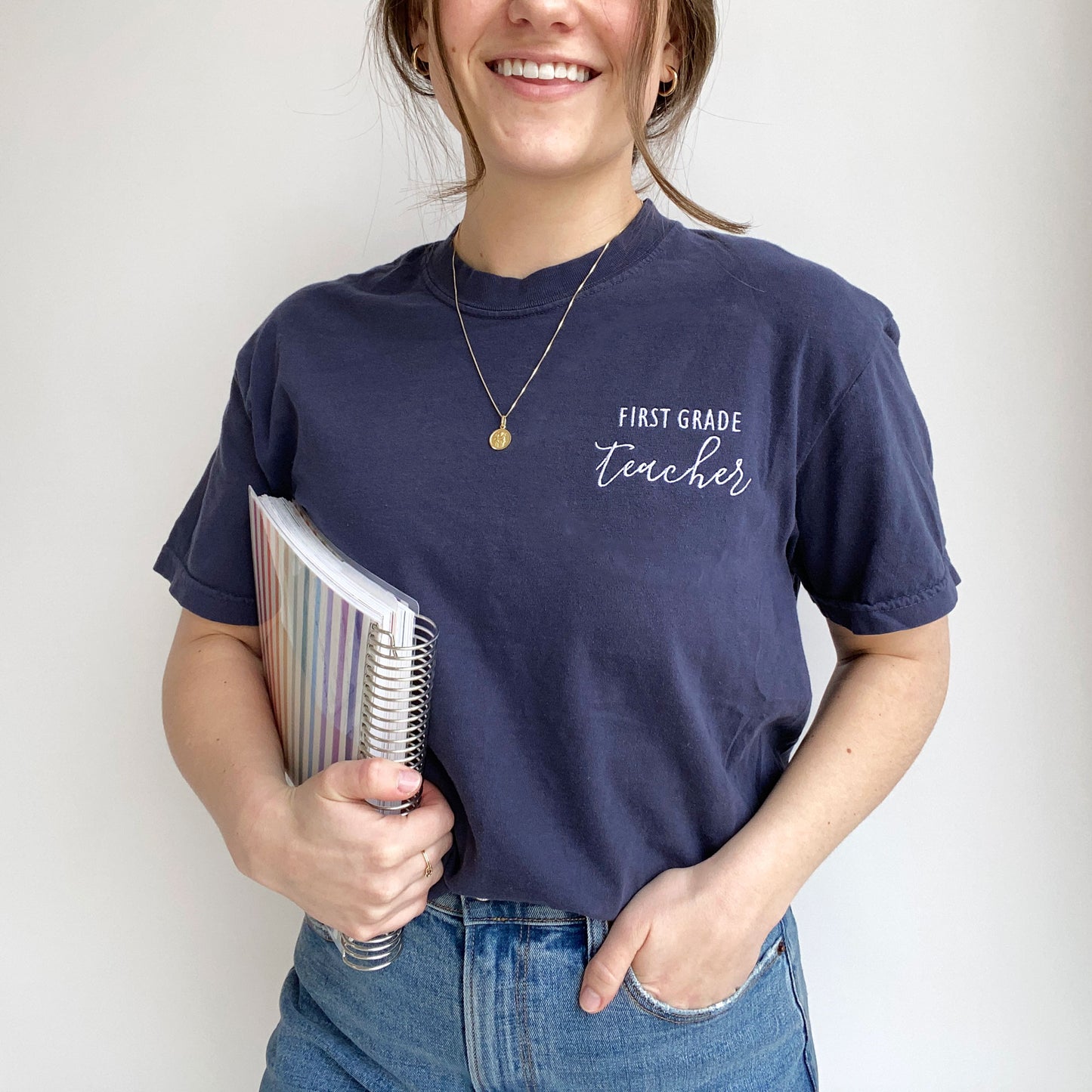 young woman modeling a nay comfort colors t-shirt with embroidered custom grade level and teacher design in white threads on the left chest