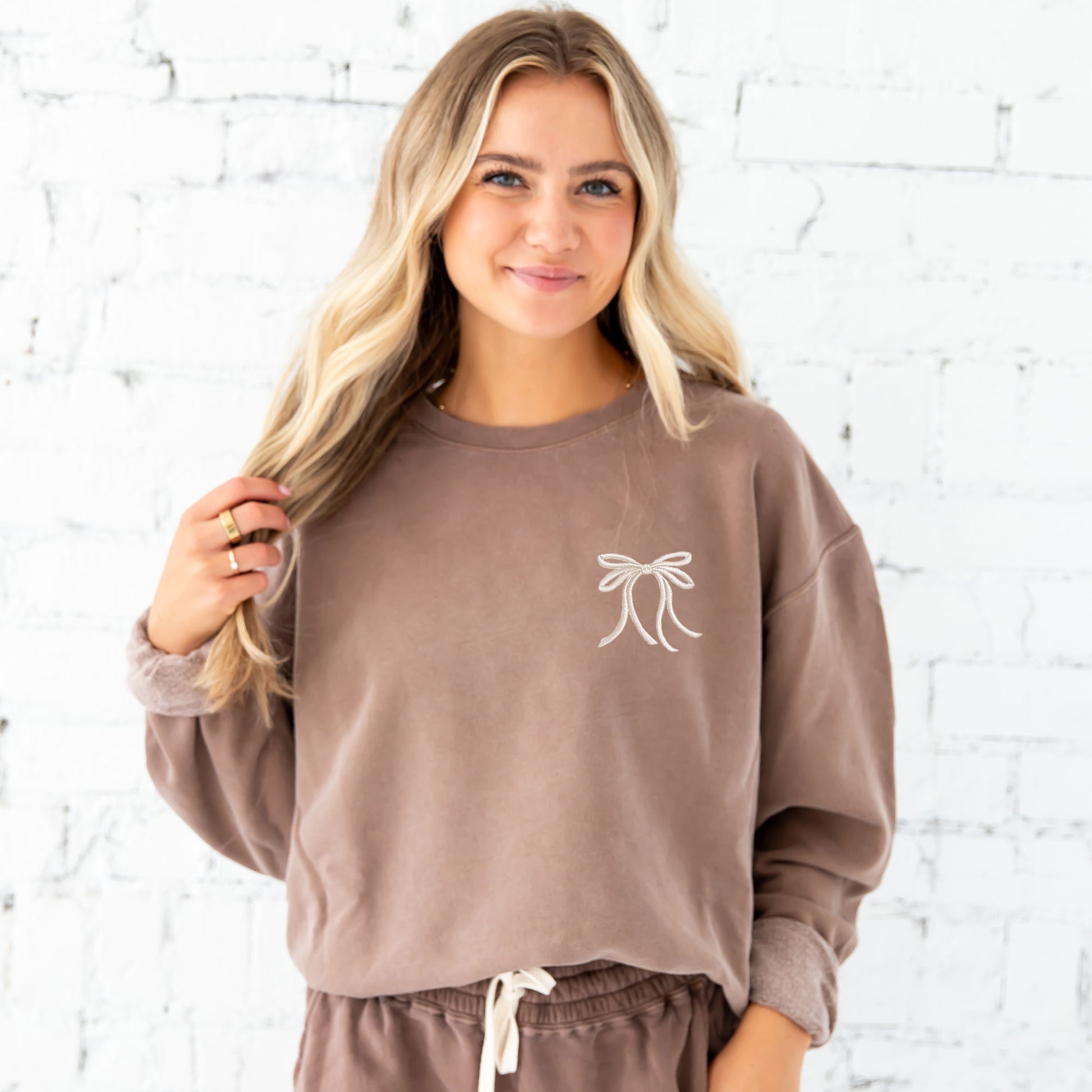 woman wearing an espresso comfort colors lightweight crewneck sweatshirt with embroidered ribbon bow on the left chest in natural thread