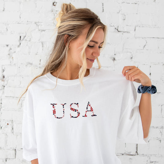 young woman wearing an oversied white comfort colors t-shirt with embroidered floral USA design in red, white, and navy threads
