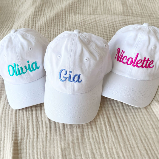 three whiet youth baseball hats with embroidered names in bright colors
