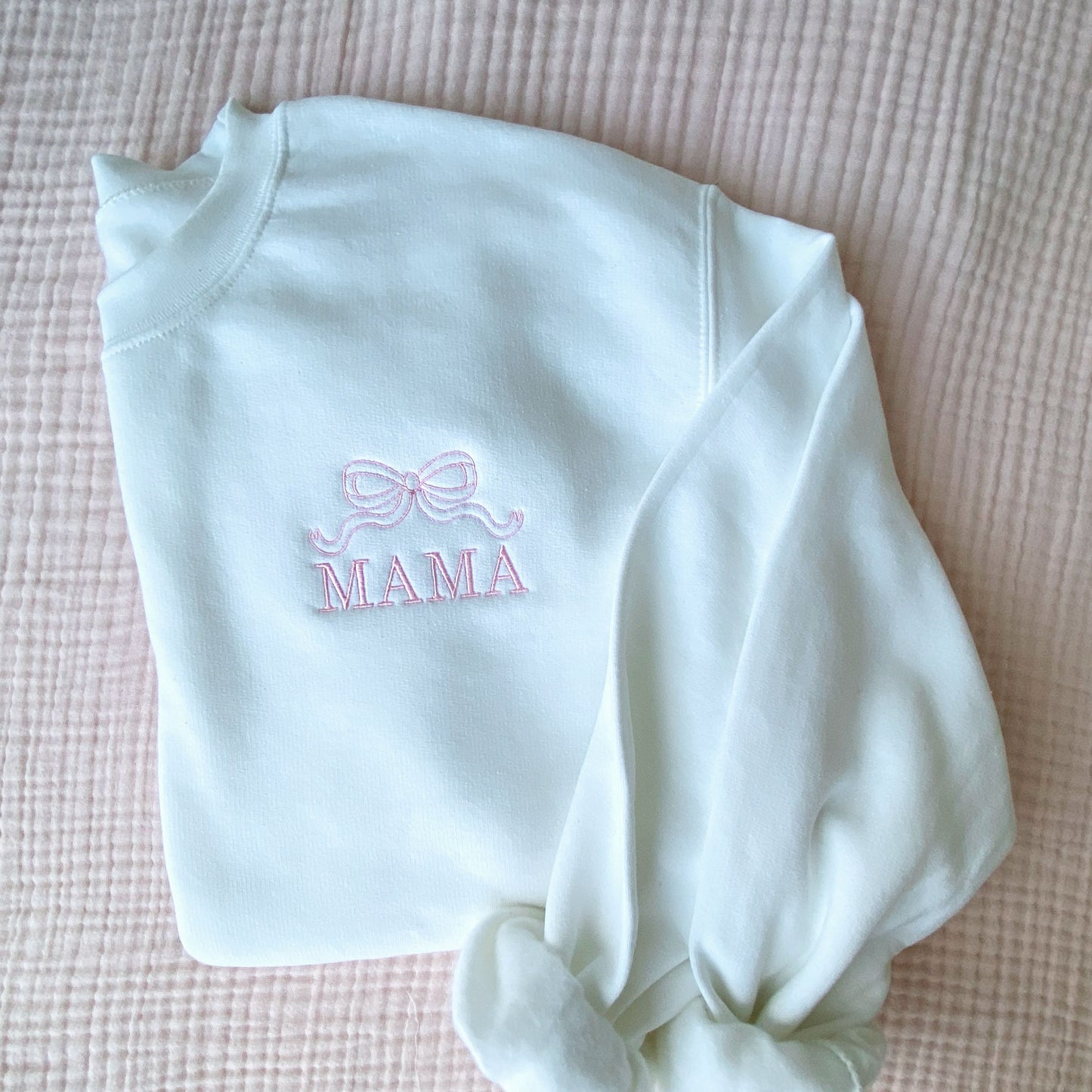 white crewneck sweatshirt with embroidered outline bow and all caps mama design on the left chest in baby pink thread