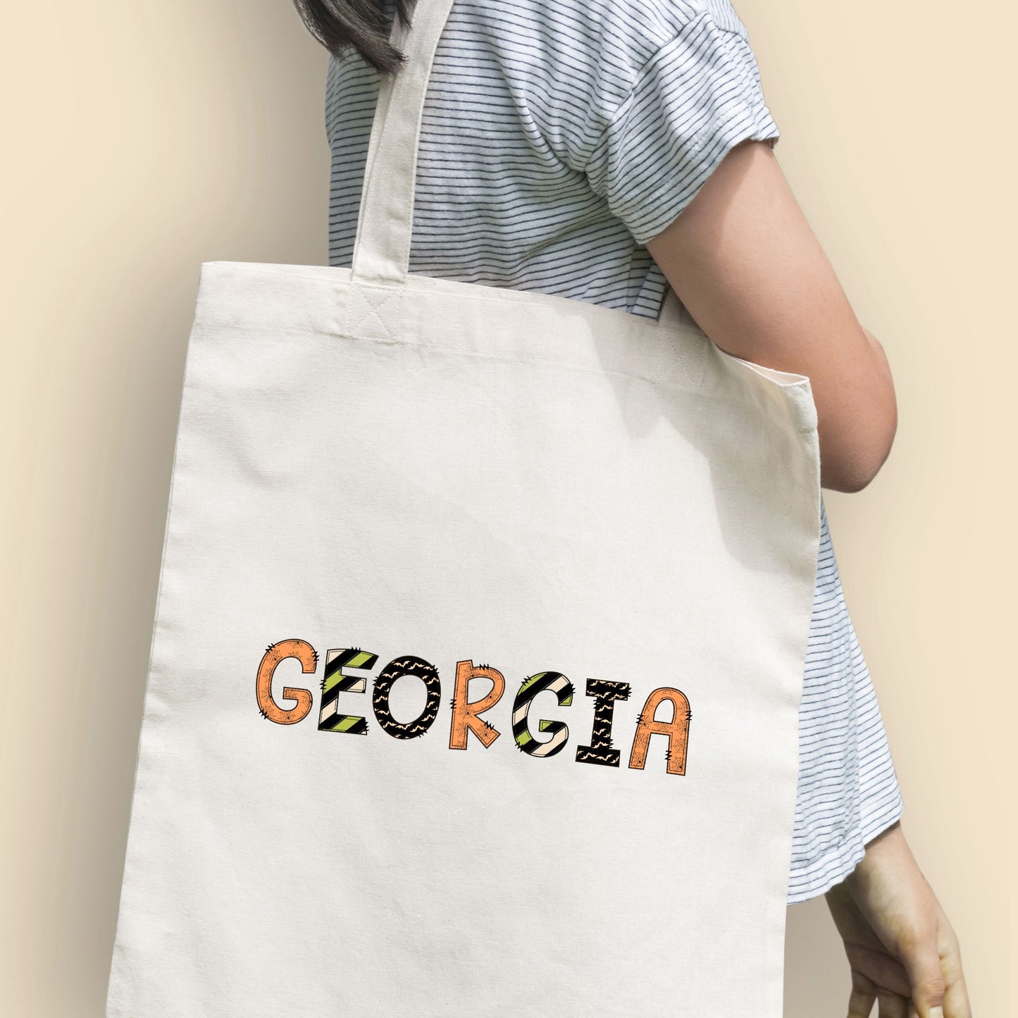 Girl holding a natural tote bag with a fun custom name print in a mixed halloween inspired pattern text.