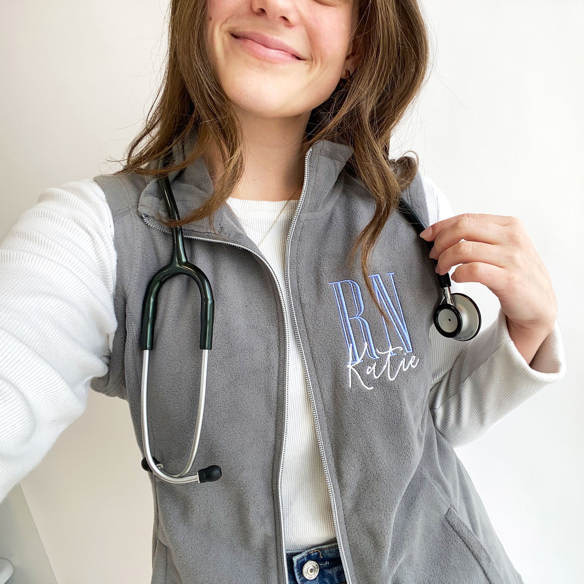 selfie of a young woman wearing a grey flecce vest with personalized RN embroidered design 