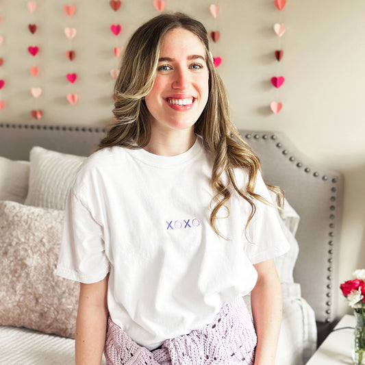 Young woman styling a white tee with mini purple xoxo design embroidered on the chest