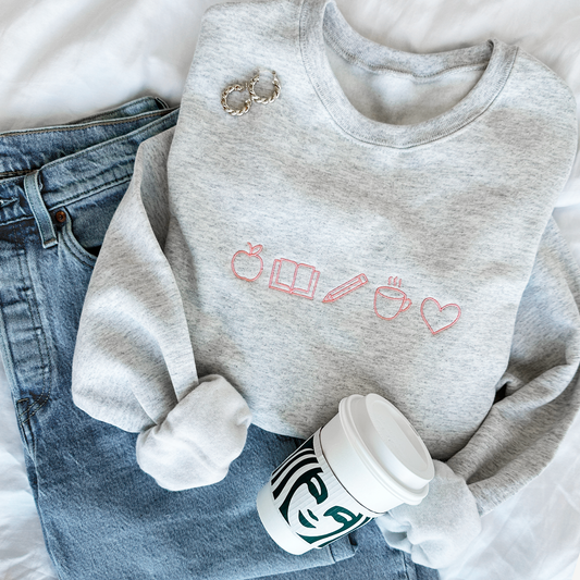 ash crewneck sweatshirt with teacher icons embroidered small across the chest in coral pink thread.