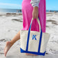 woman walking on a beach carrying a medium canvas tote with an embroidered shadow block initial design