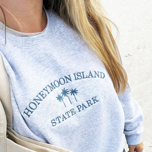 woman on a beach wearing an ash gray sweatshirt with honeymoon island embroidered across the front