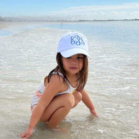 young girl playing on a beach with a white baseball cap with embroidered monogram in periwinkle thread