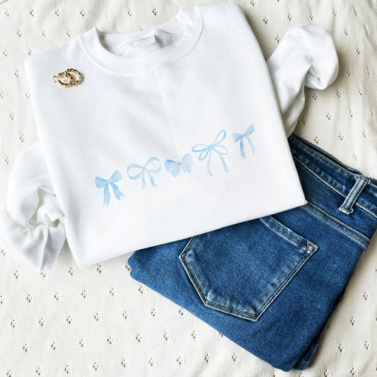 white sweatshirt with mini watercolor bow printed design across the chest paired with jeans and gold hoop earrings