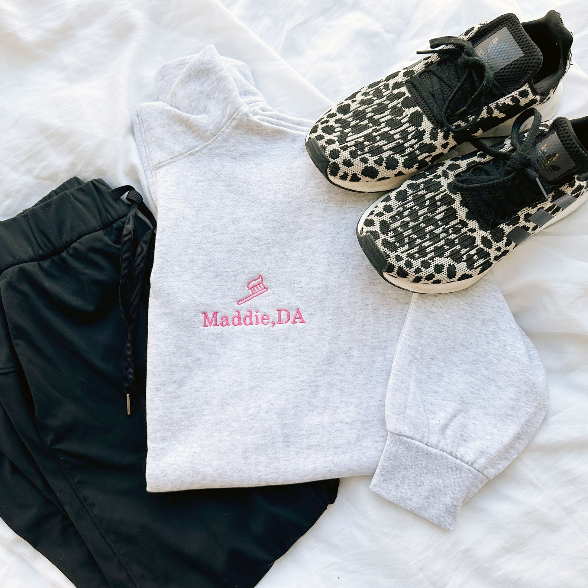 ash quarterzip sweatshirt with pink embroidered tooth brush and name Maddie, DA on the left chest  styled with black scrubs and sneakers