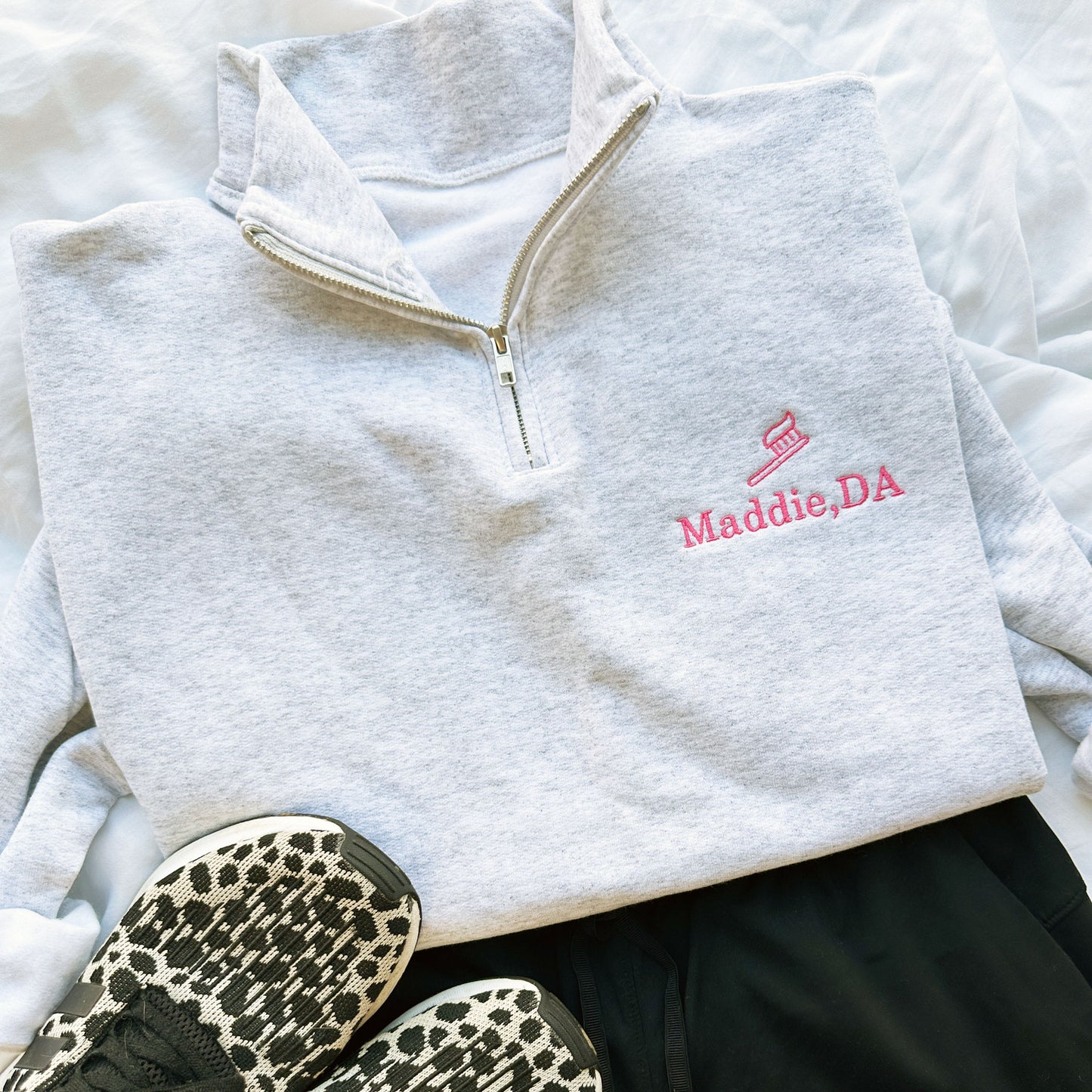 ash quarterzip sweatshirt with pink embroidered tooth brush and name Maddie, DA on the left chest  styled with black scrubs and sneakers