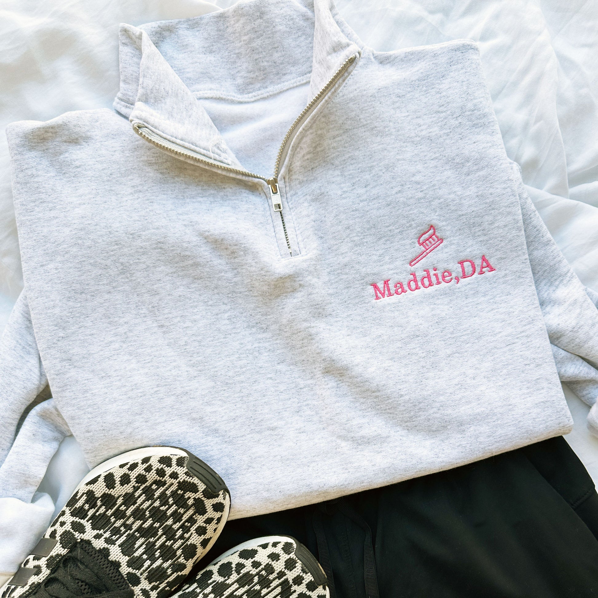 ash quarterzip sweatshirt with pink embroidered tooth brush and name Maddie, DA on the left chest  styled with black scrubs and sneakers