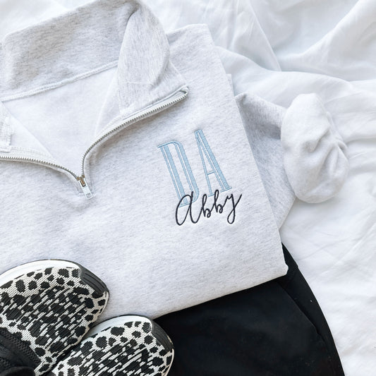 embroidered ash quarter zip sweatshirt with DA in baby blue thread and large outline letters and name Abby below DA in navy thread and a loose script font