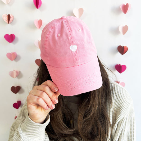 Woman wearing a pink baseball hat with a mini white embroidered heart