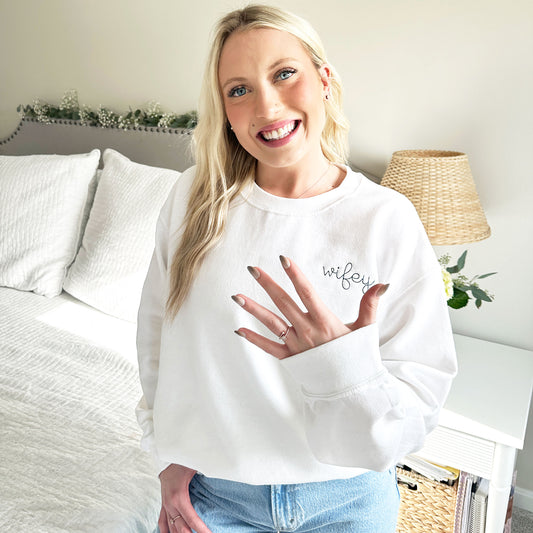 yooung woman wearing a white crewneck sweatshirt with wifey embroidered in french blue thread
