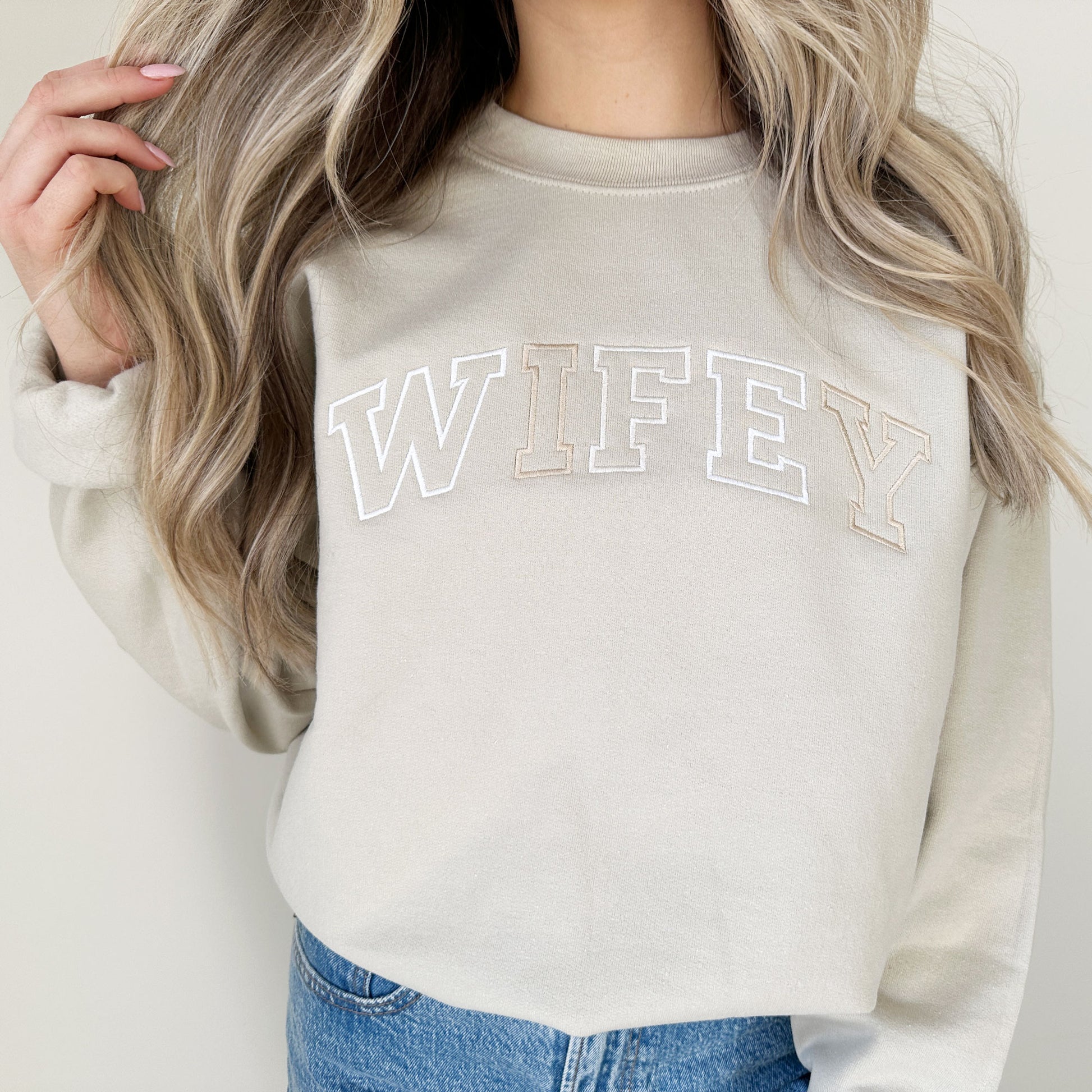 girl wearing a crewneck sweatshirt with a custom WIFEY varsity font embroidered design in neutral threads.