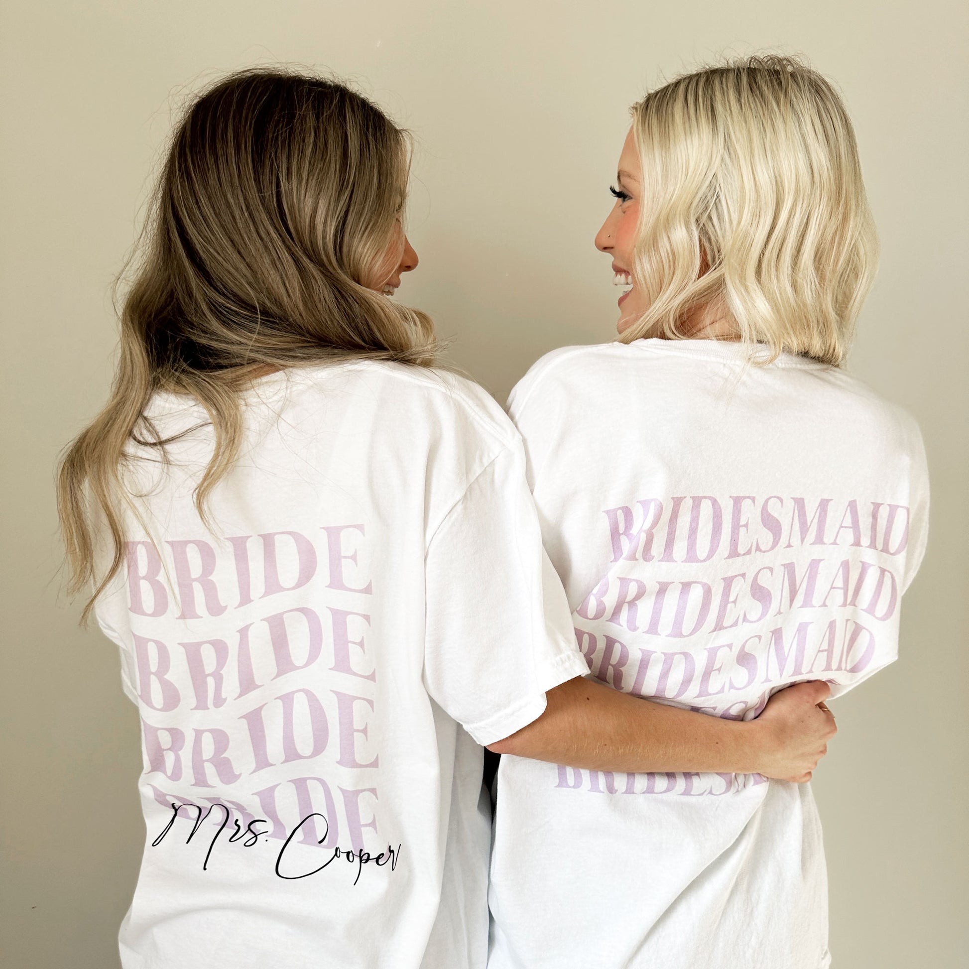 two women wearing oversized white comfort colors t-shirts with custom bride and bridesmaid printed designs on the back