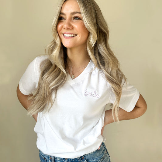 young woman wearing a white vneck tee with bride embroidered small on the left chest in lilac thread