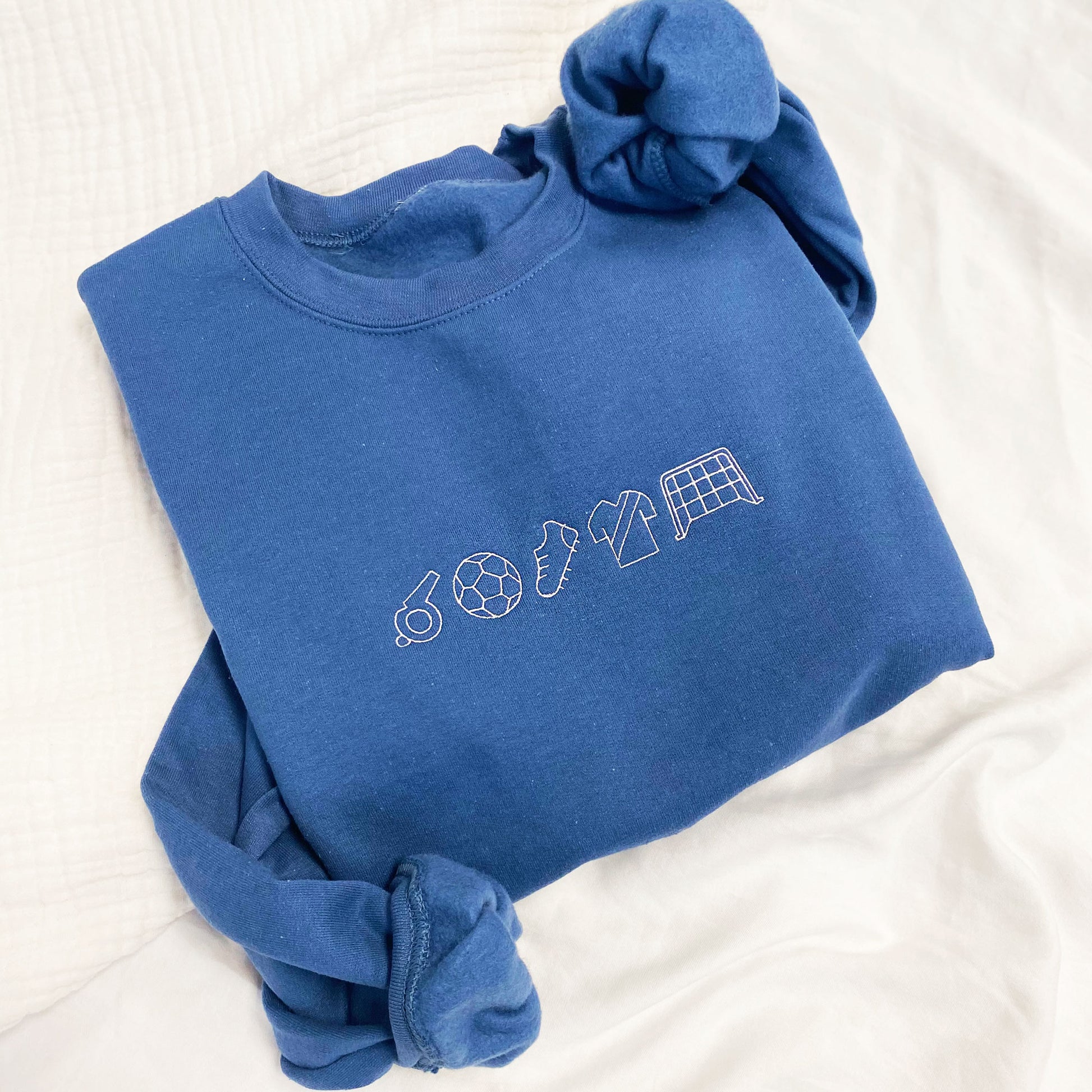 Close up of embroidered indigo crewnec sweatshirt with soccer icons in white thread