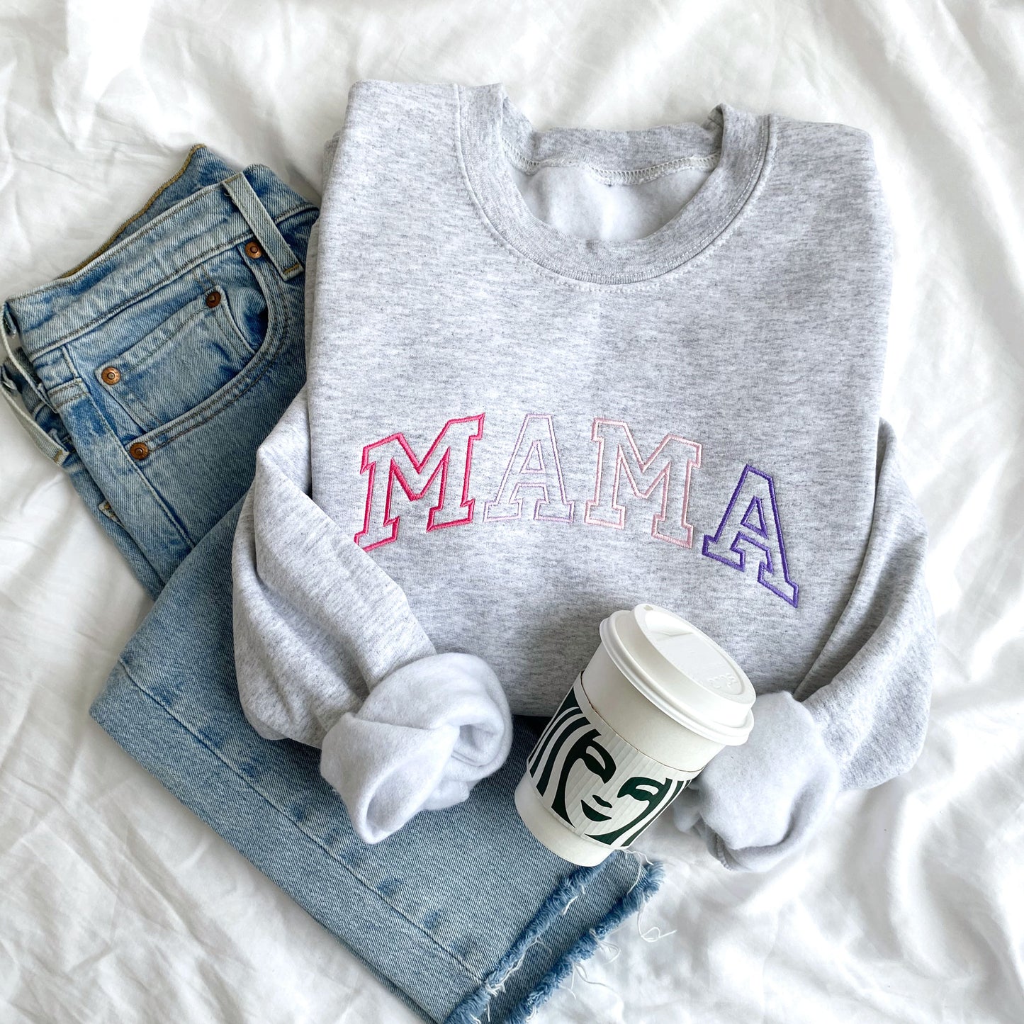 styled flat lay of an ash crewneck sweatshirt with embroidered athletic block mama in alternating shades of pink and purple