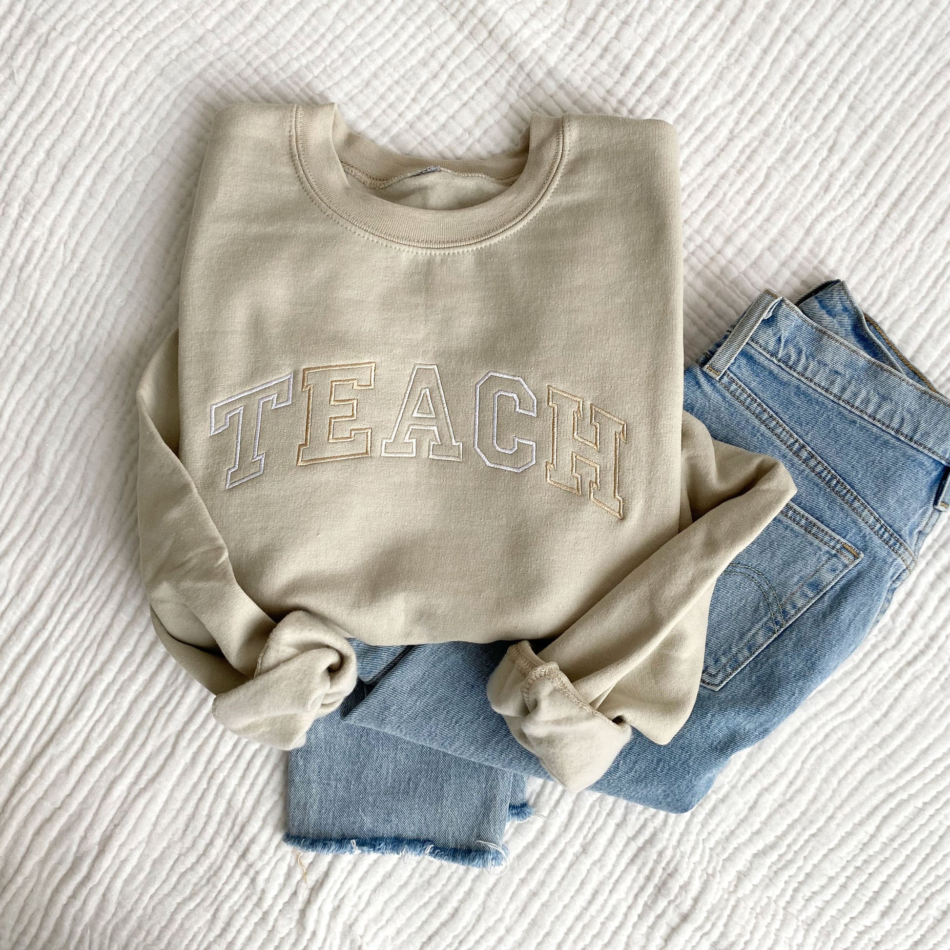 flat lay of a sand crewneck sweatshirt with embroidered neutral color block teach design across the chest