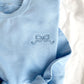 close up of mini outlined bow in french blue thread embroidered on a light blue crewneck sweatshirt