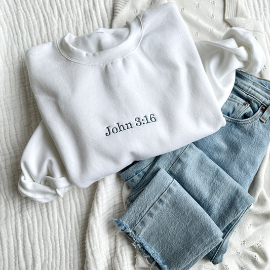 white crewneck sweatshirt with bible verse John 3:16 embroidered in french blue thread styled with blue jeans