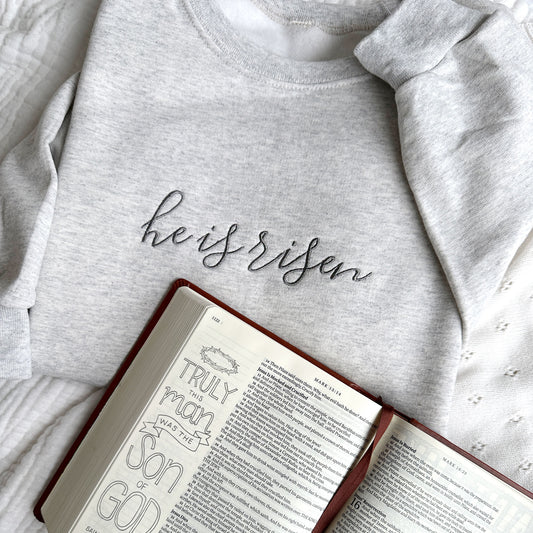 Embroidered crewneck sweatshirt with he is risen embroidered in gray thread styled with a bible