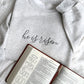 Embroidered crewneck sweatshirt with he is risen embroidered in gray thread styled with a bible