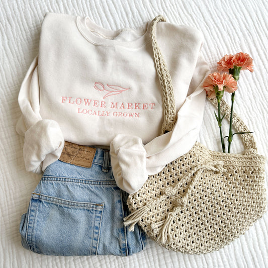 styled lat lay of a sweet cream flower maket embroidered crewneck sweatshirt with jeans and a tote bag with live flowers