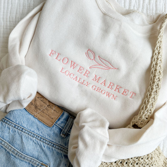 Sweet cream crewneck sweatshirt with a tulip design above flower makert locally grown embroidered text in coral pink thread