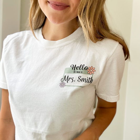 Woman wearing a white comfort colors t-shirt with a custom daisy name tag print featuring a name in a script font