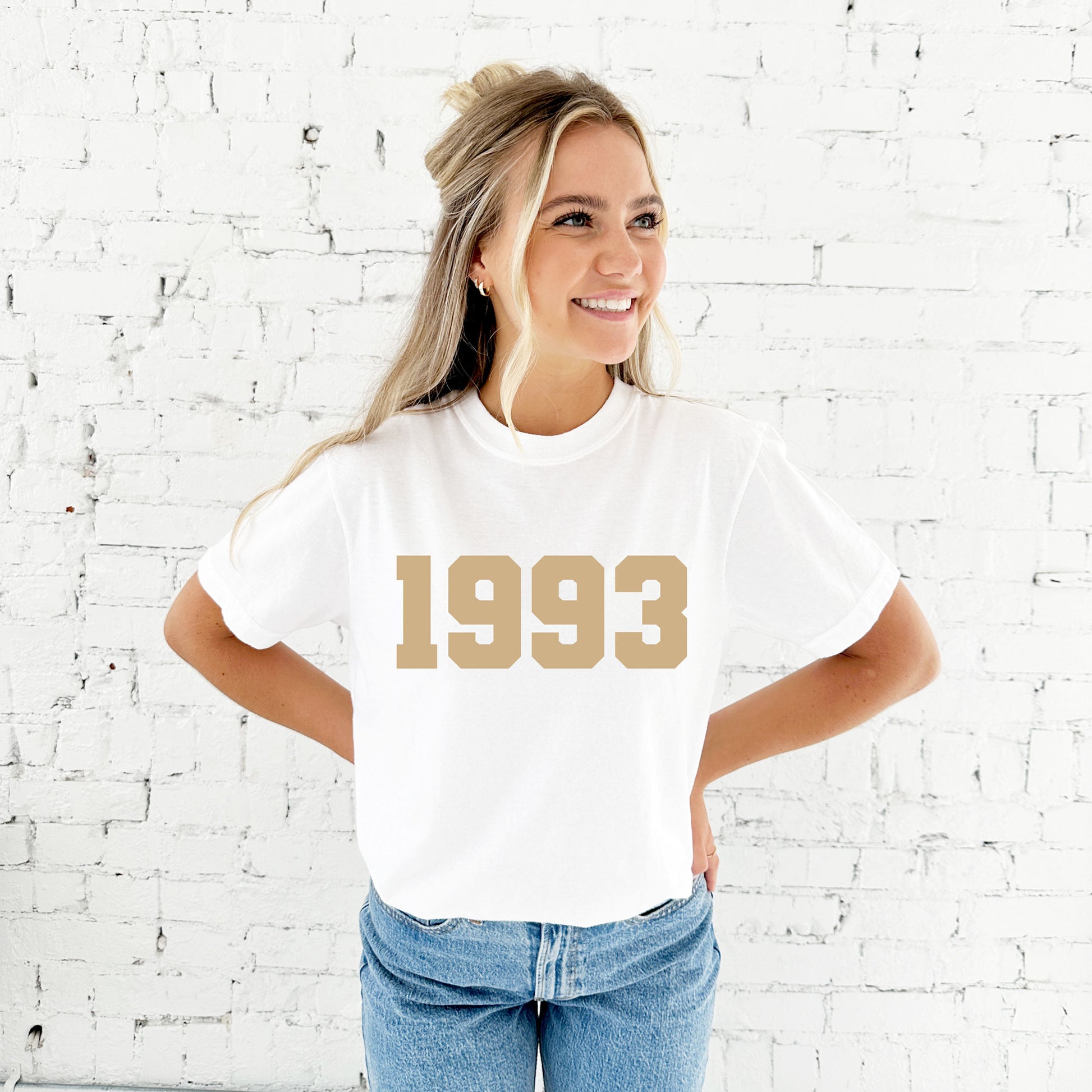 girl wearing a white comfort colors tee with a custom birth year printed design in a camel ink