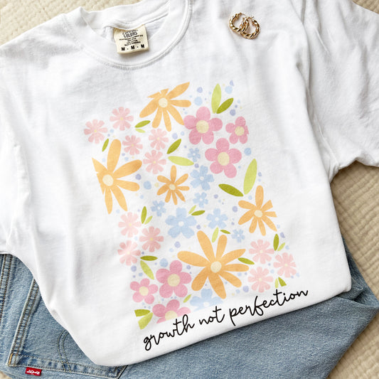 white comfort colors tee with a playful floral print and growth not perfection in a script underneath