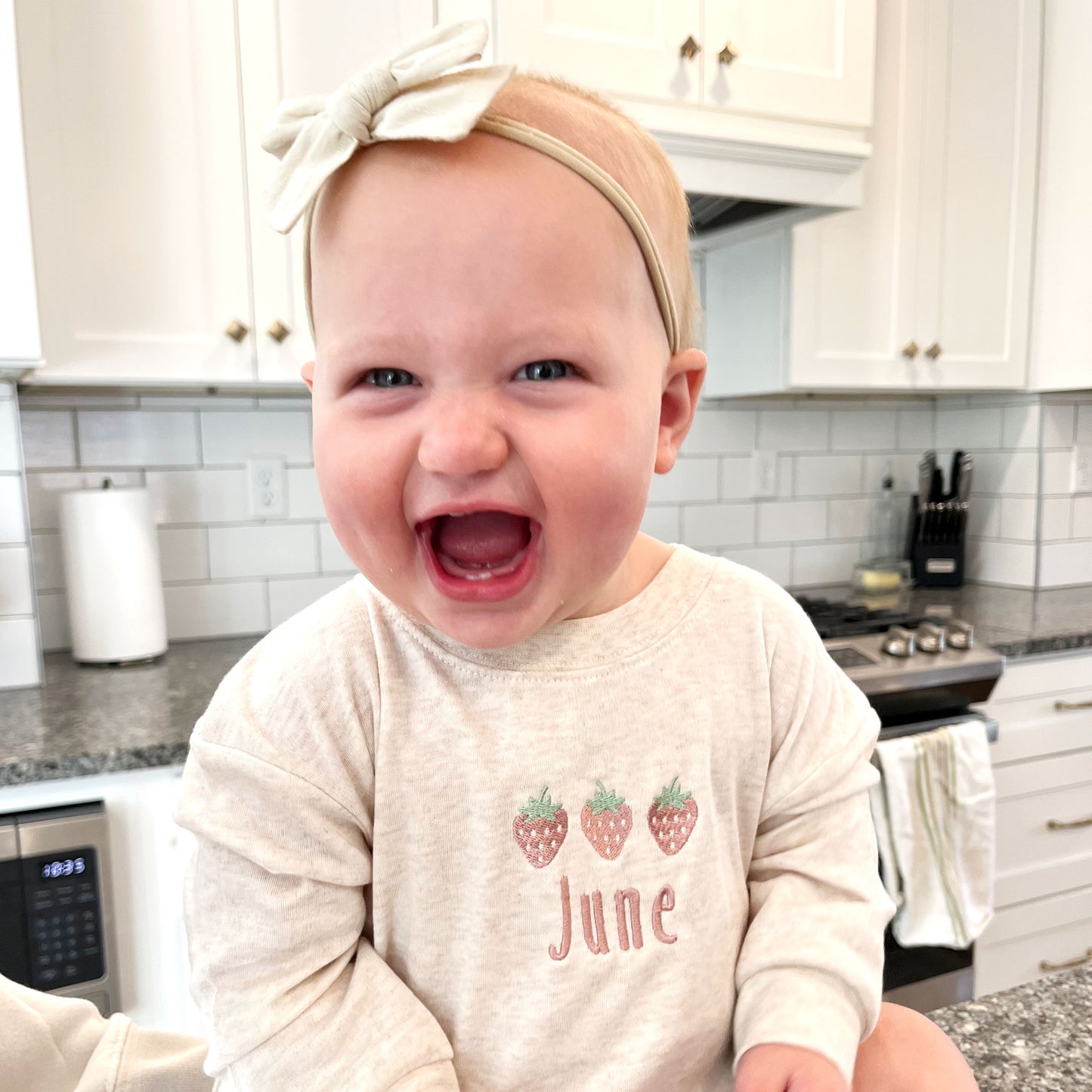baby girl wearing an oat bubble romper with custom strawberry and name embroidered design