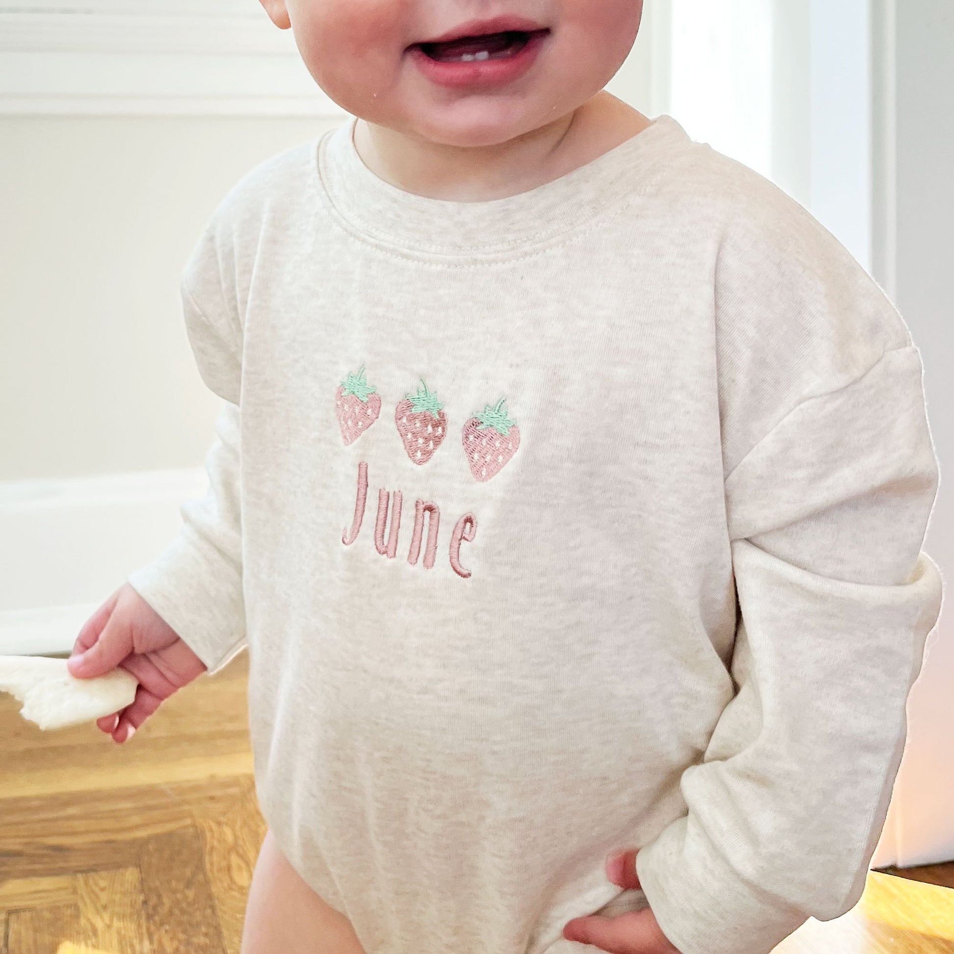 baby girl wearing an oat bubble romper with custom strawberry and name embroidered design